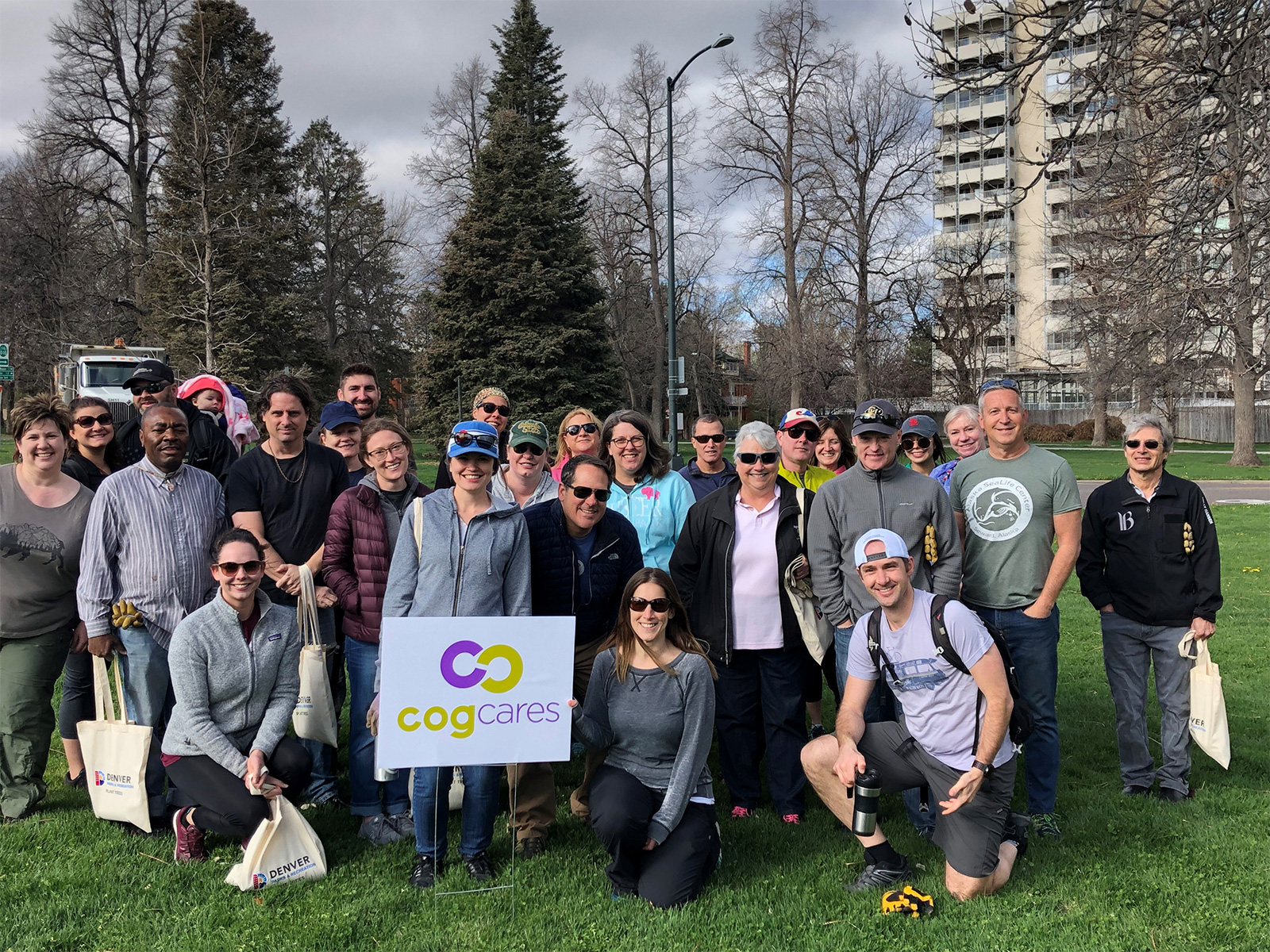 A large group of people standing in a park in front of a sign that says Cog Cares.
