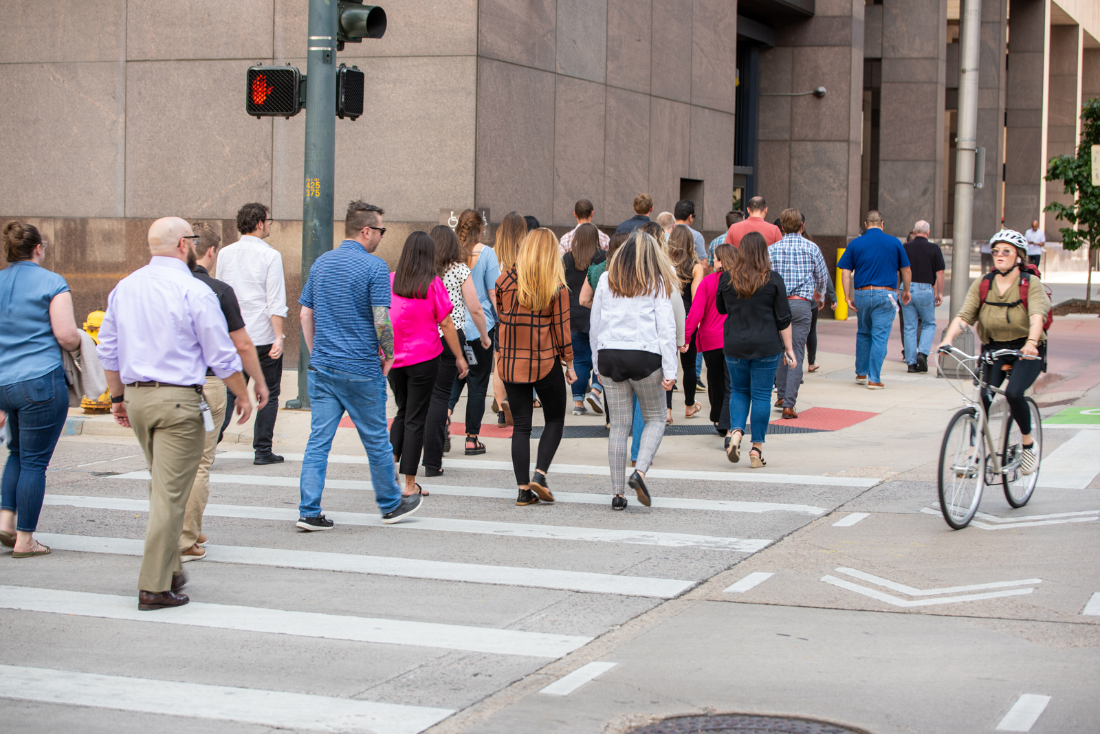 A group of people crossing a crosswalk on a city street next to a cyclist riding a bike in a bike lane.