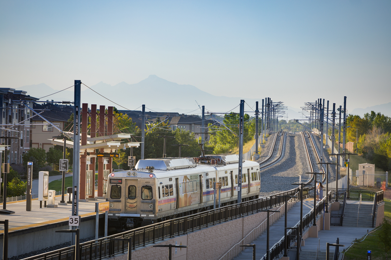 A commuter rail train pulling into a suburban station with hazy mountains in the background. Photo credit: Photo courtesy of RTD.