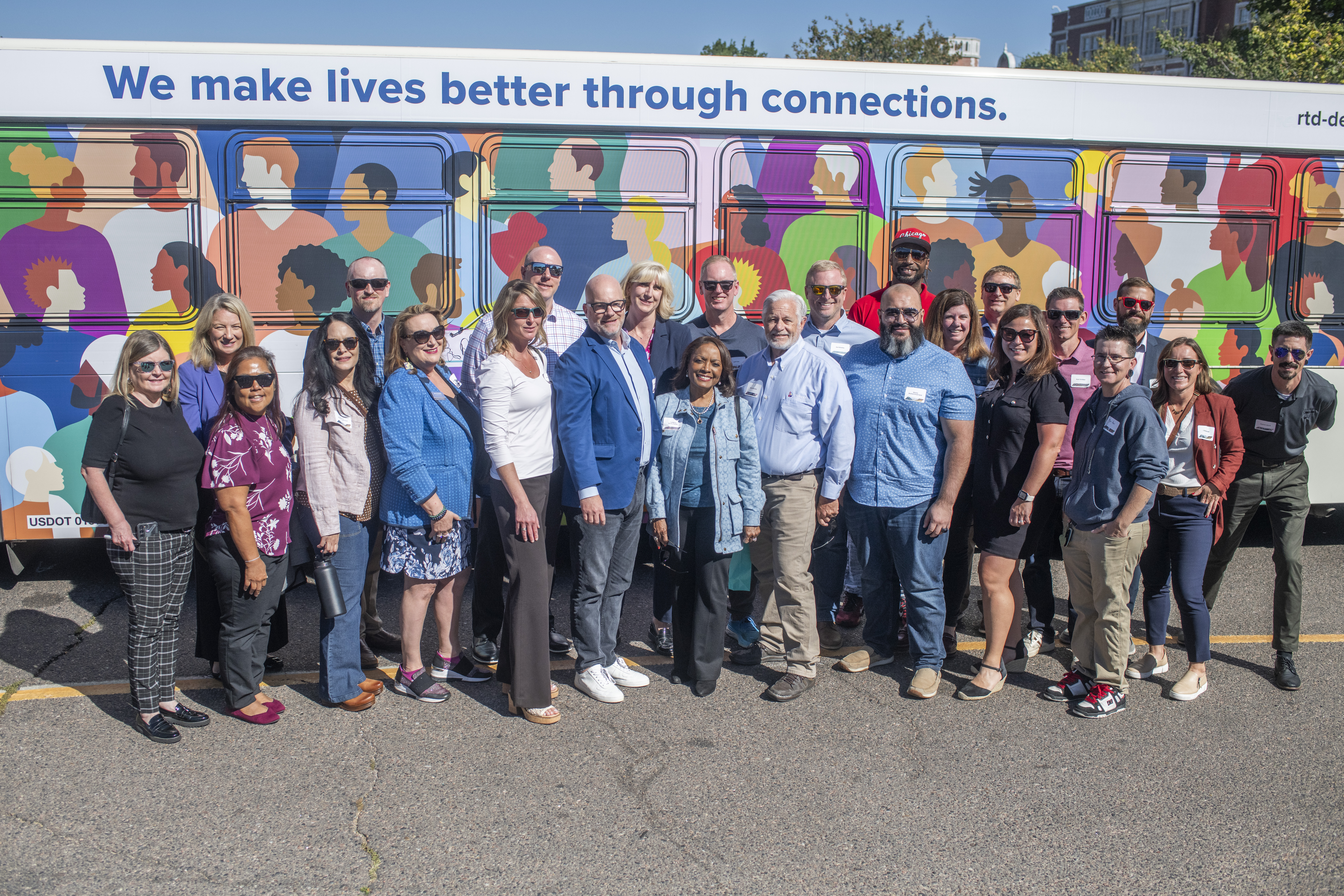 A diverse group of people stand in front of a bus. 
